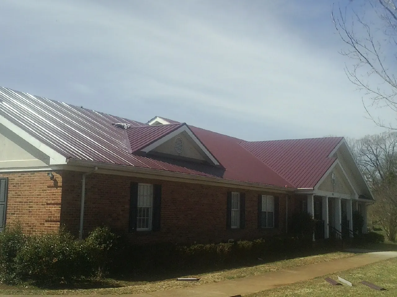 Red metal roof with gabled entries on a long brick building, from a Hail Damage Roof Repair job in Ledyard