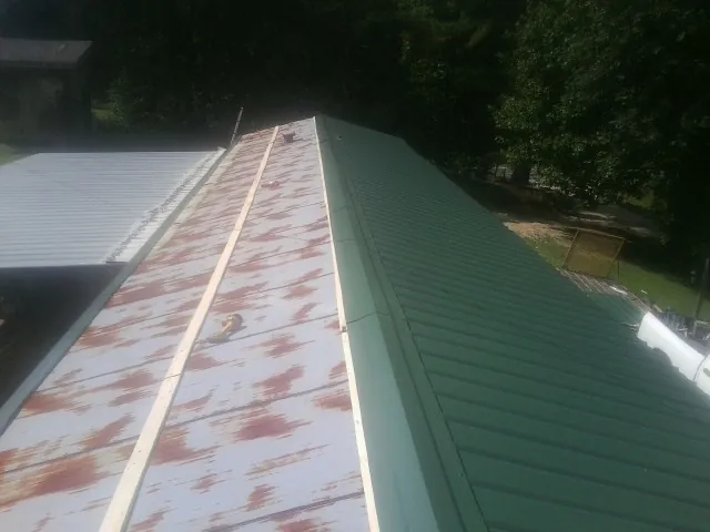 Old rusted panels beside newly installed green metal roofing — Wind Damage Roof Repair by Roofing Brothers in Ledyard