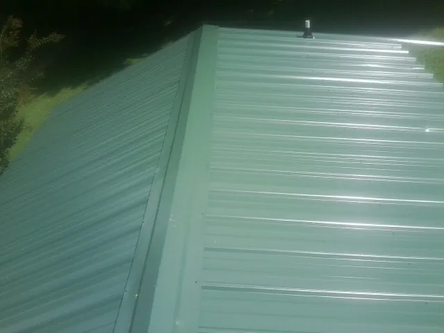 New green metal panels meeting at the ridge of a roof — Flat Roof Repair work by our crew in Ledyard