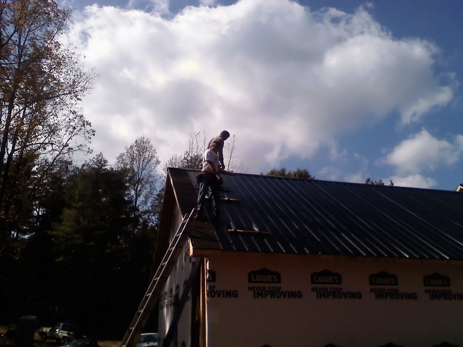 Roofer fastening dark metal panels high against a cloudy sky, from a Roof Inspection job in Ledyard