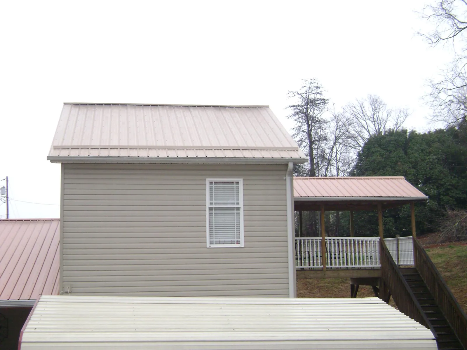 Tan metal roofs on a two story addition and attached porch, from a Roof Replacement job in Ledyard